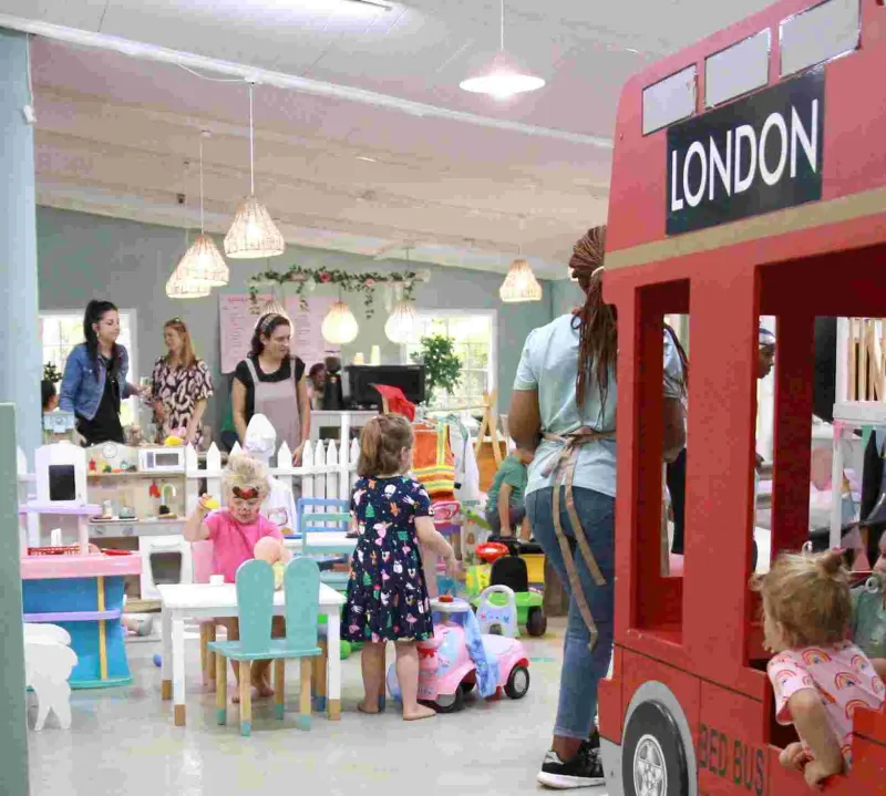 Children playing in colorful indoor play area beside red London bus prop