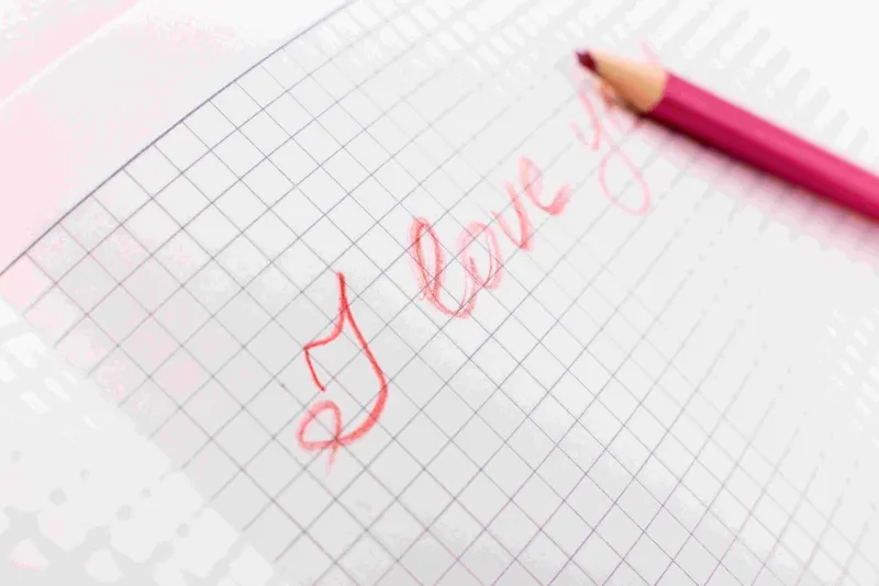 pink pencil resting on grid notebook with I love you written in red