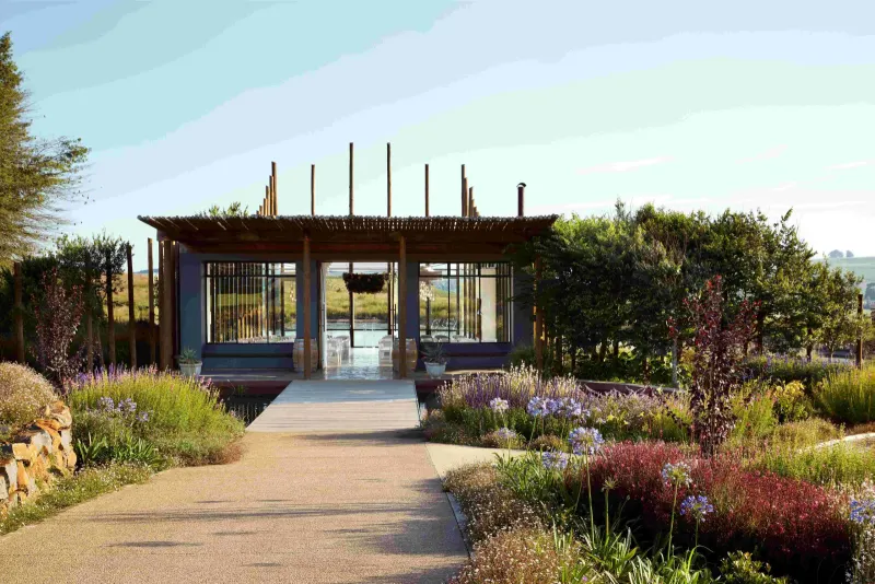 Pathway lined with purple wildflowers leading to an open pergola structure surrounded by lush gardens