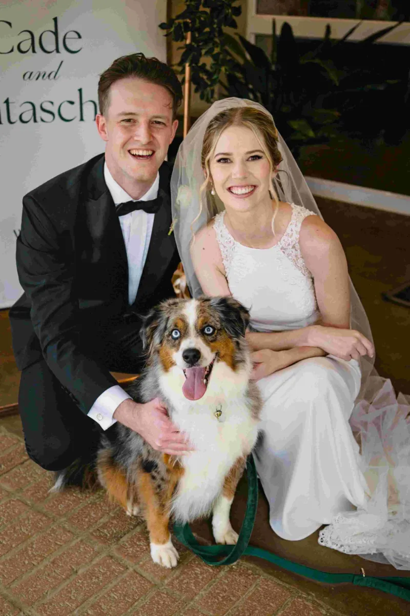 smiling bride and groom posing with an Australian Shepherd dog on their wedding day