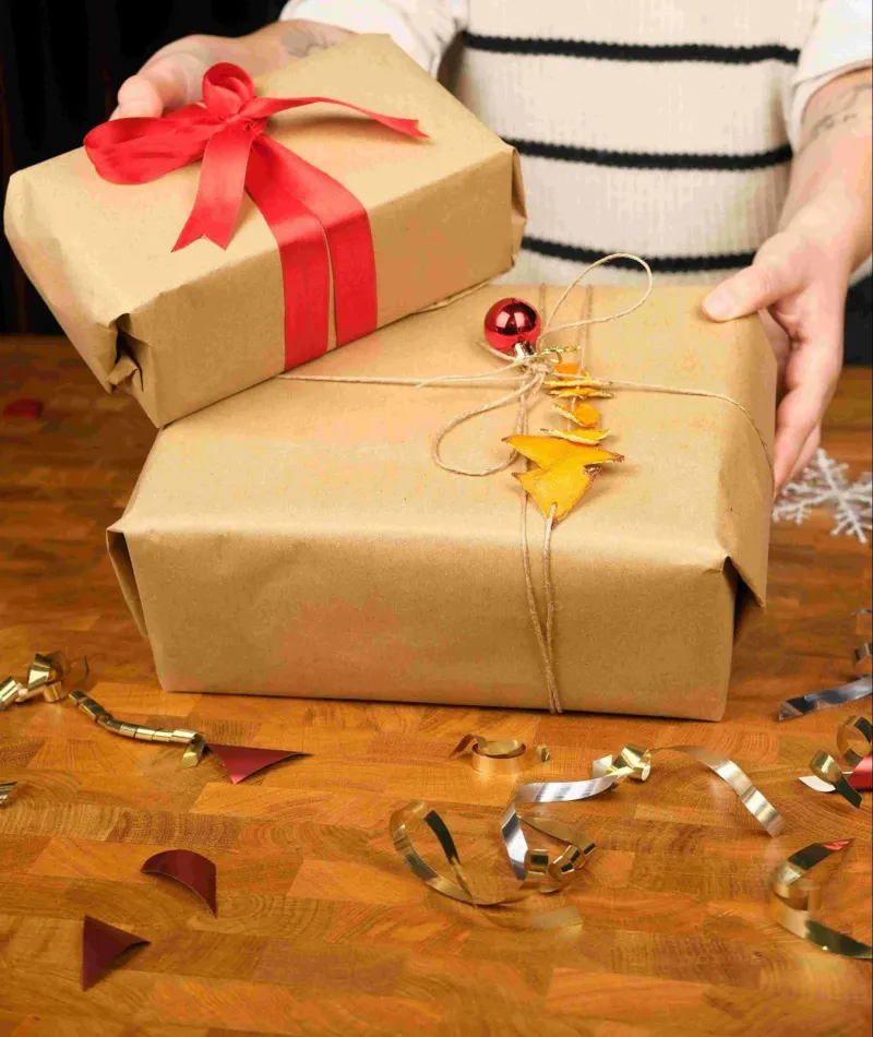 Person holding two kraft paper wrapped gifts with red ribbon bow and twine decorations